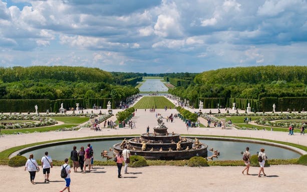 Visitors exploring the gardens and fountain at the Palace of Versailles, France.