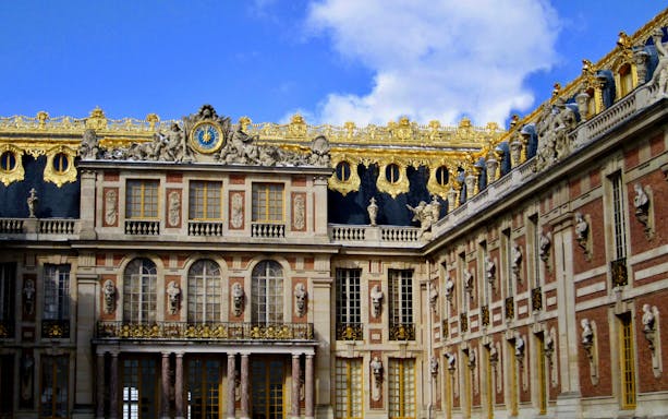 Palace of Versailles facade with ornate gold detailing and sculptures.
