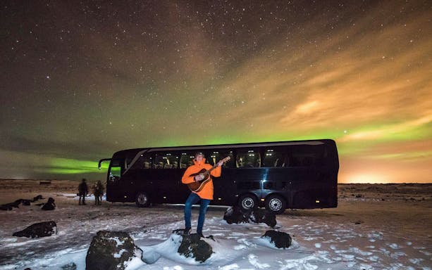 Bus tour under Northern Lights near Reykjavik, person playing guitar in snow.