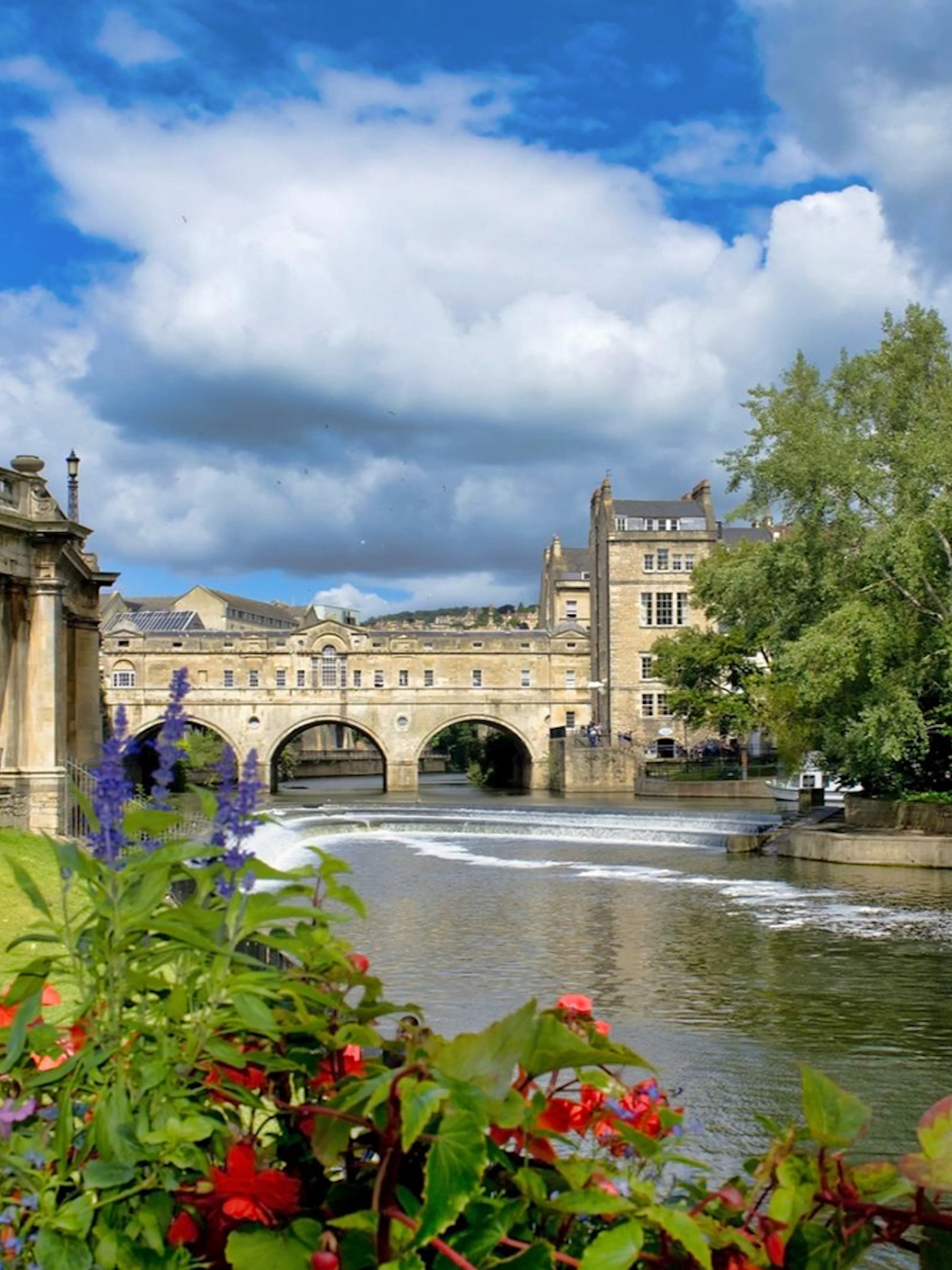 Pulteney Bridge over River Avon in Bath, surrounded by flowers and historic architecture.