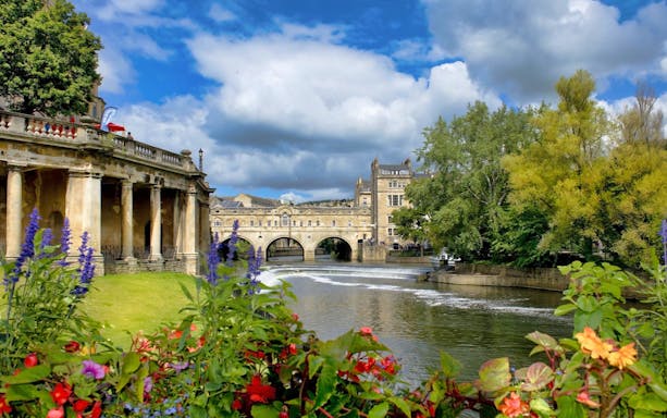 Pulteney Bridge over River Avon in Bath, surrounded by flowers and historic architecture.
