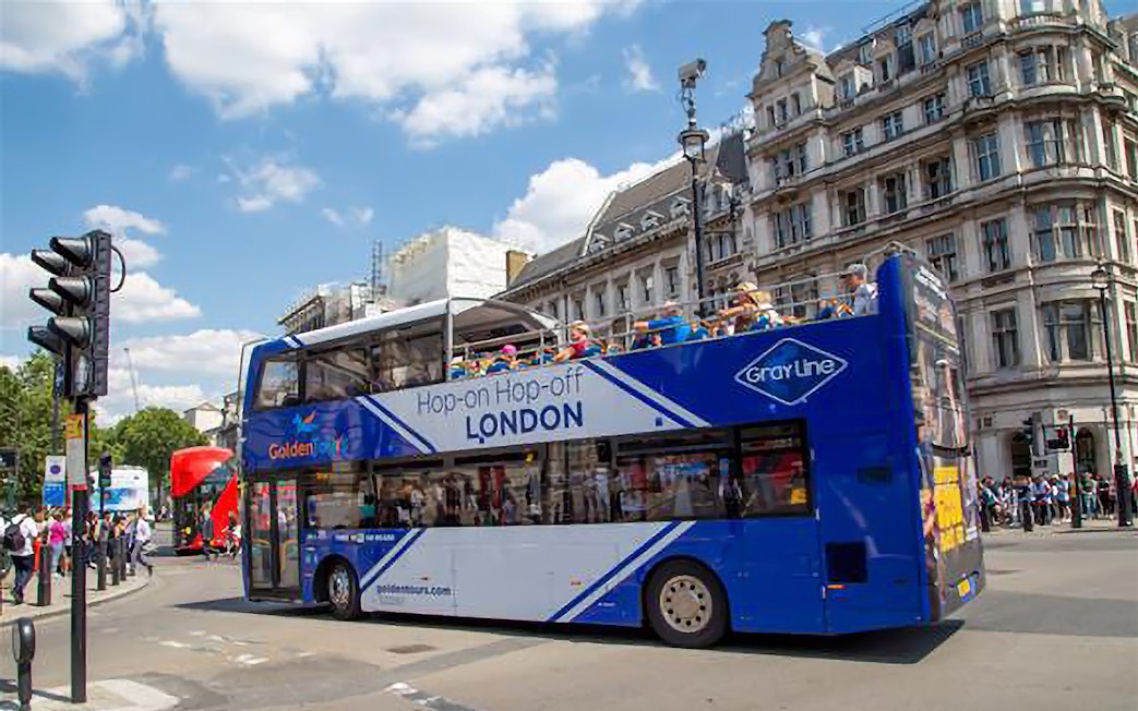 Open-top London tour bus on city street near historic buildings.