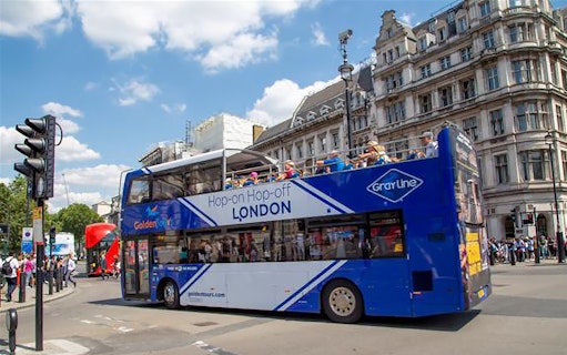 Open-top London tour bus on city street near historic buildings.