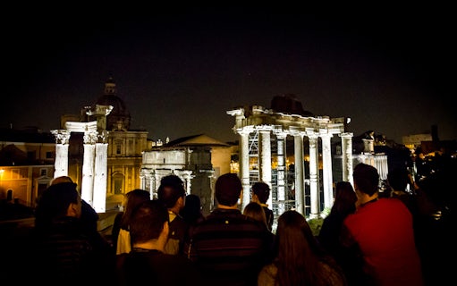 Tour group viewing illuminated Roman Forum ruins at night in Rome.