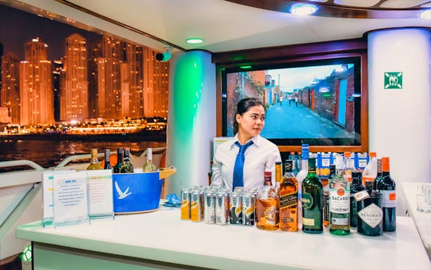 Bartender on Lotus Mega Yacht with drinks selection, Dubai Marina skyline at night.