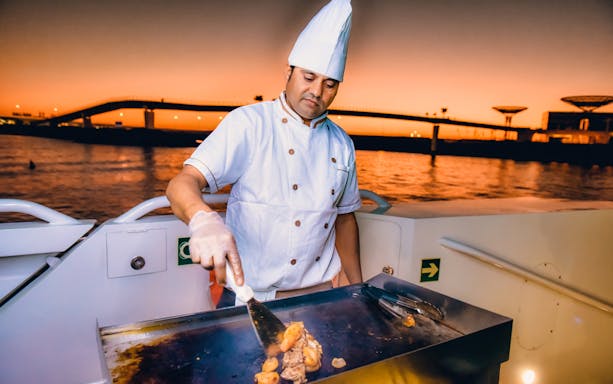 Chef grilling food on Lotus Mega Yacht during sunset brunch cruise.