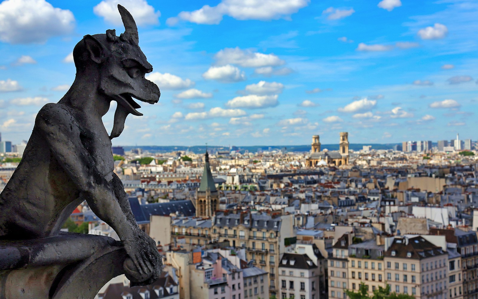 Gargoyle overlooking Paris from Notre Dame with cityscape and Île de la Cité in view.