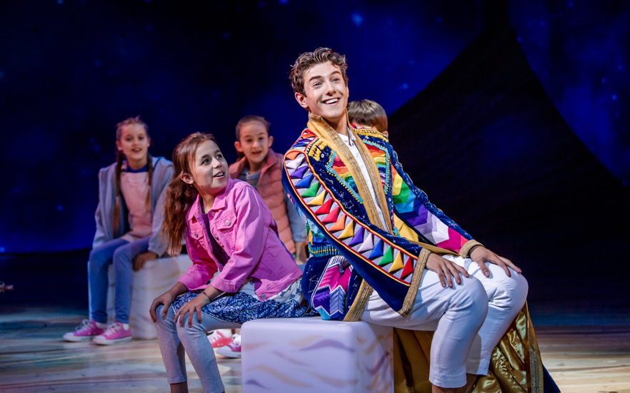 Young performer in colorful coat with children on stage in Joseph musical.