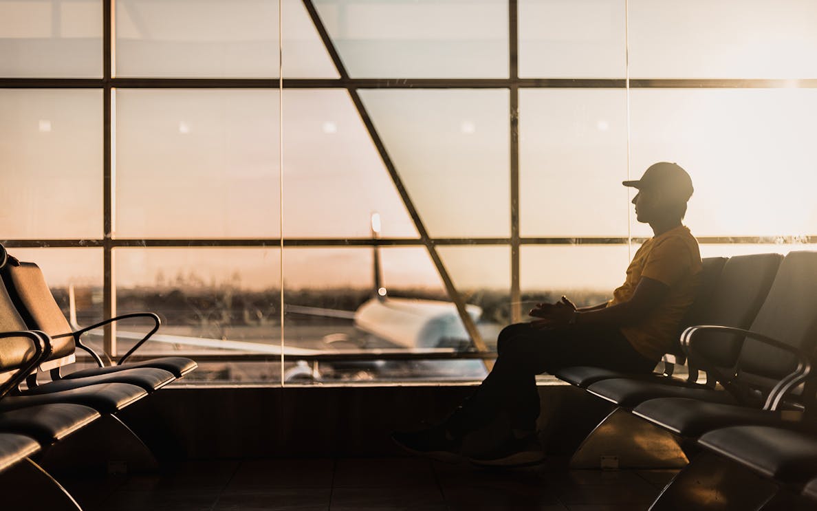 Traveler waiting at Dubai airport terminal during sunset, airplane visible through window.