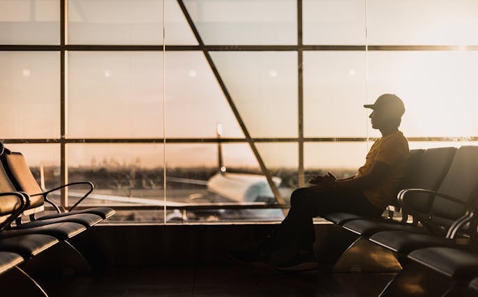 Traveler waiting at Dubai airport terminal during sunset, airplane visible through window.