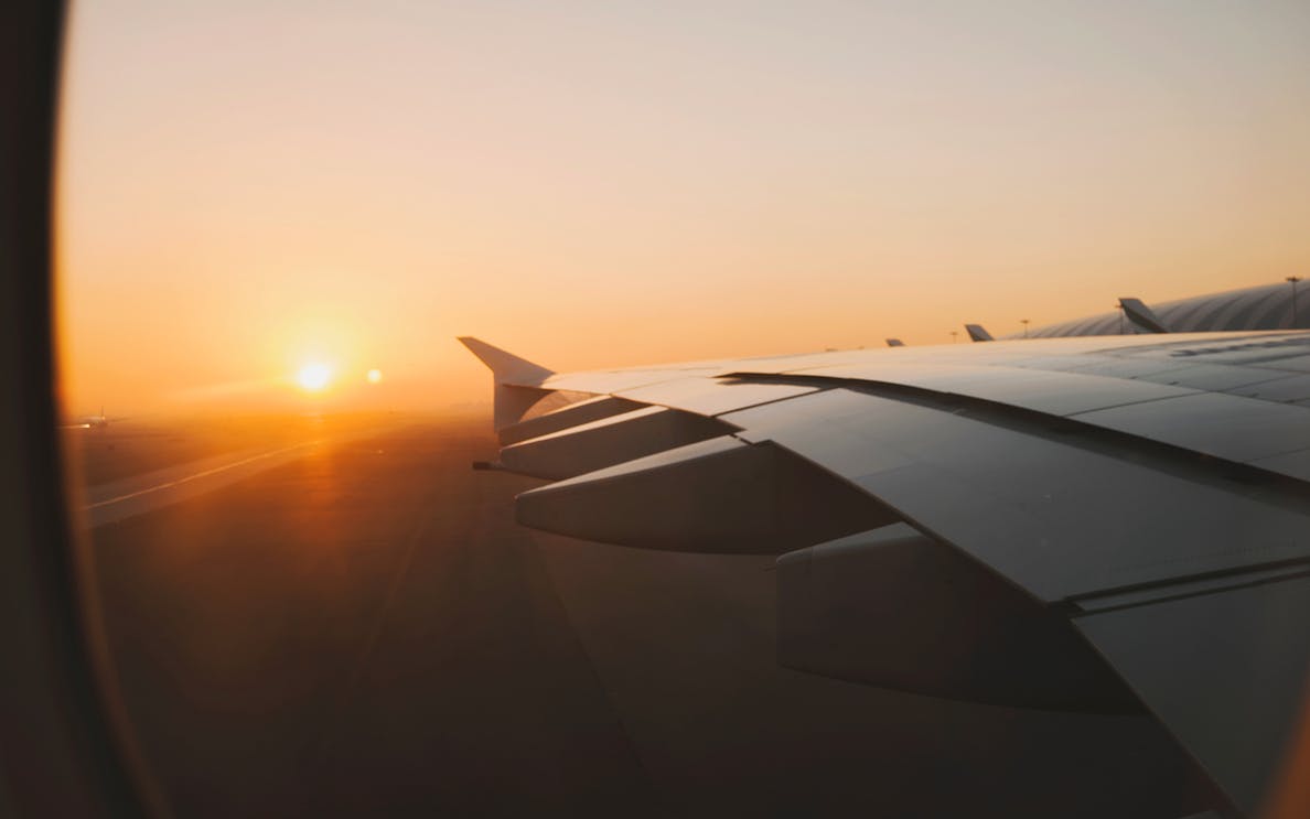 Airplane wing over Dubai at sunrise, highlighting private transfer service.