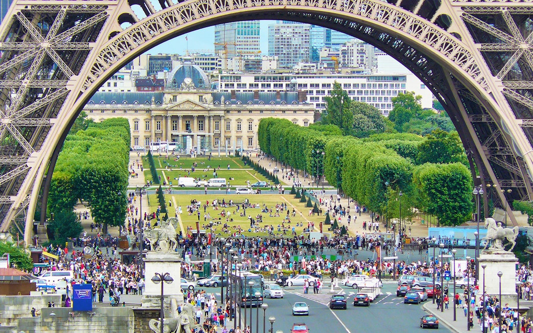 View of Champ de Mars from Eiffel Tower, Paris, with crowds and cityscape in the background.