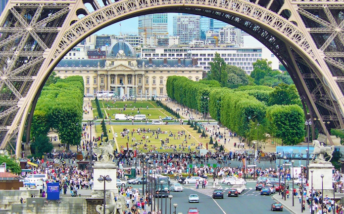 View of Champ de Mars from Eiffel Tower, Paris, with crowds and cityscape in the background.