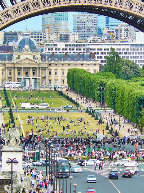 View of Champ de Mars from Eiffel Tower, Paris, with crowds and cityscape in the background.