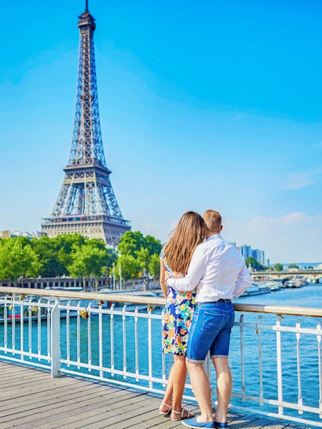 Couple enjoying view of Eiffel Tower from Seine River bridge, Paris.