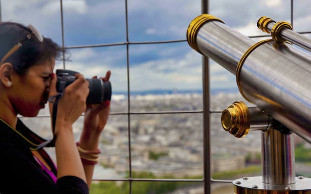 Person photographing Paris from Eiffel Tower's second floor observation deck.