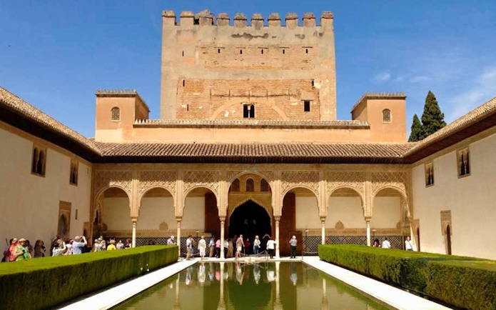 Visitors at Alhambra's Nasrid Palaces courtyard with reflecting pool, Granada, Spain.