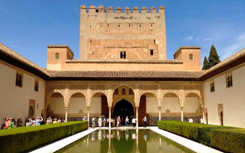 Visitors at Alhambra's Nasrid Palaces courtyard with reflecting pool, Granada, Spain.