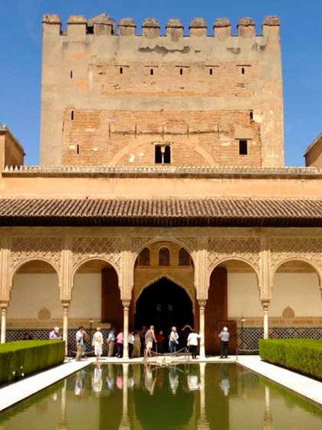 Visitors at Alhambra's Nasrid Palaces courtyard with reflecting pool, Granada, Spain.