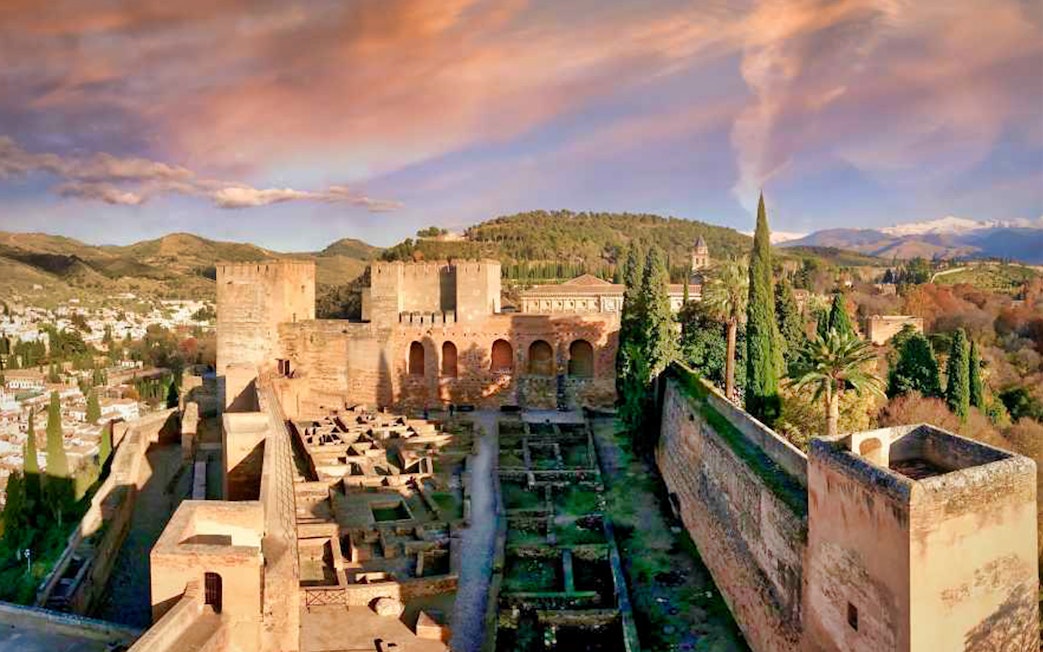 Alhambra fortress with Nasrid Palaces in Granada, Spain, surrounded by lush greenery and mountains.