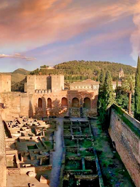 Alhambra fortress with Nasrid Palaces in Granada, Spain, surrounded by lush greenery and mountains.