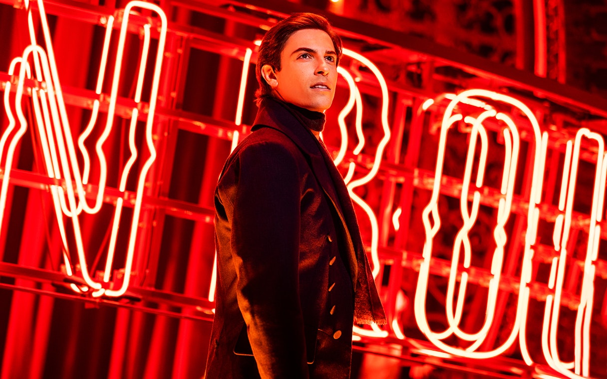 Performer in front of Moulin Rouge neon sign during the musical.