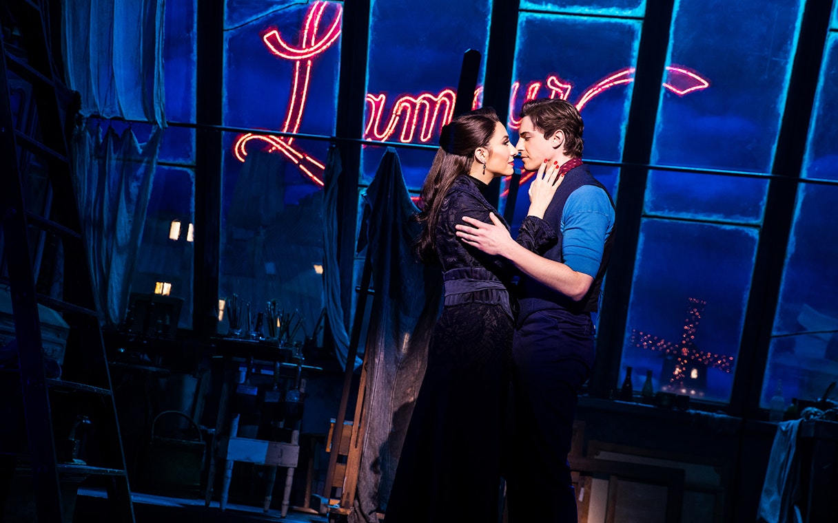 Couple embracing on stage with Moulin Rouge sign in background.