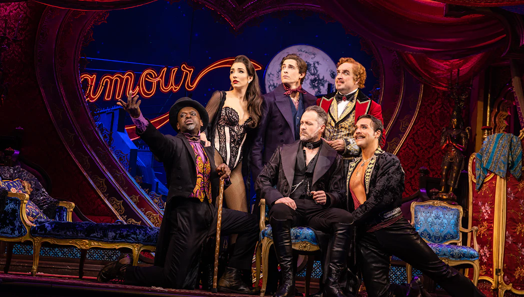 Cast of Moulin Rouge! The Musical on stage with vibrant set design.