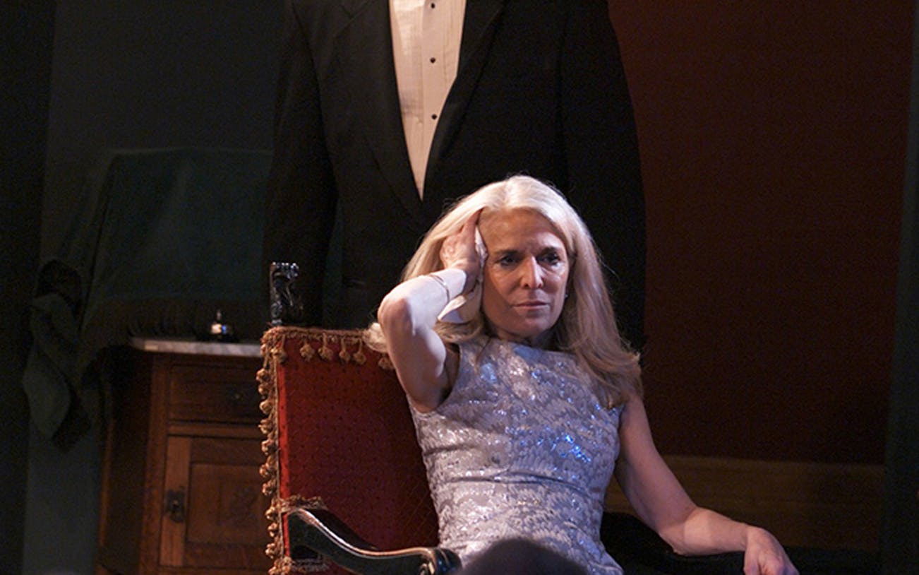 Woman in a silver dress sitting in a red chair, part of the "Perfect Crime" theater scene.