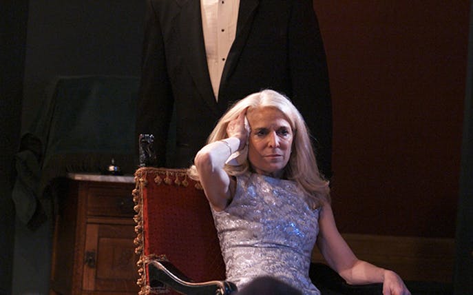 Woman in a silver dress sitting in a red chair, part of the "Perfect Crime" theater scene.