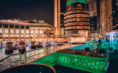 Mega yacht deck with dining setup, Dubai Marina skyline at night.