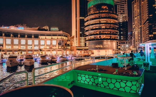 Mega yacht deck with dining setup, Dubai Marina skyline at night.