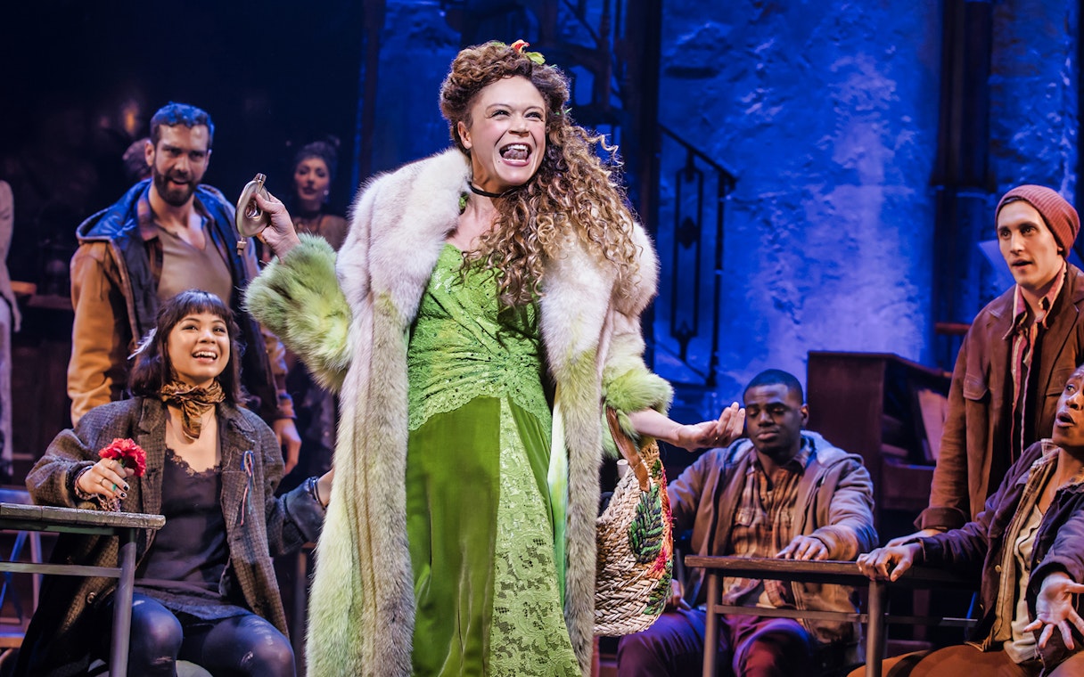 Performer in Hadestown musical on stage with cast members.