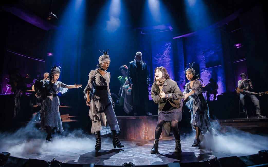 Performers on stage during a Hadestown musical scene with dramatic lighting.