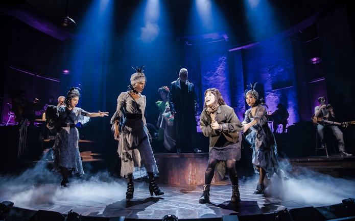 Performers on stage during a Hadestown musical scene with dramatic lighting.
