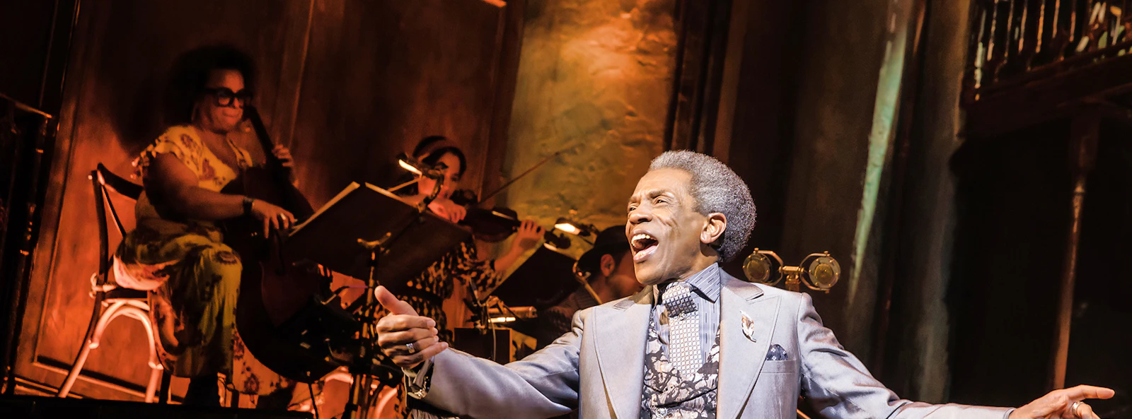 Performer singing on stage during Hadestown musical with musicians in the background.