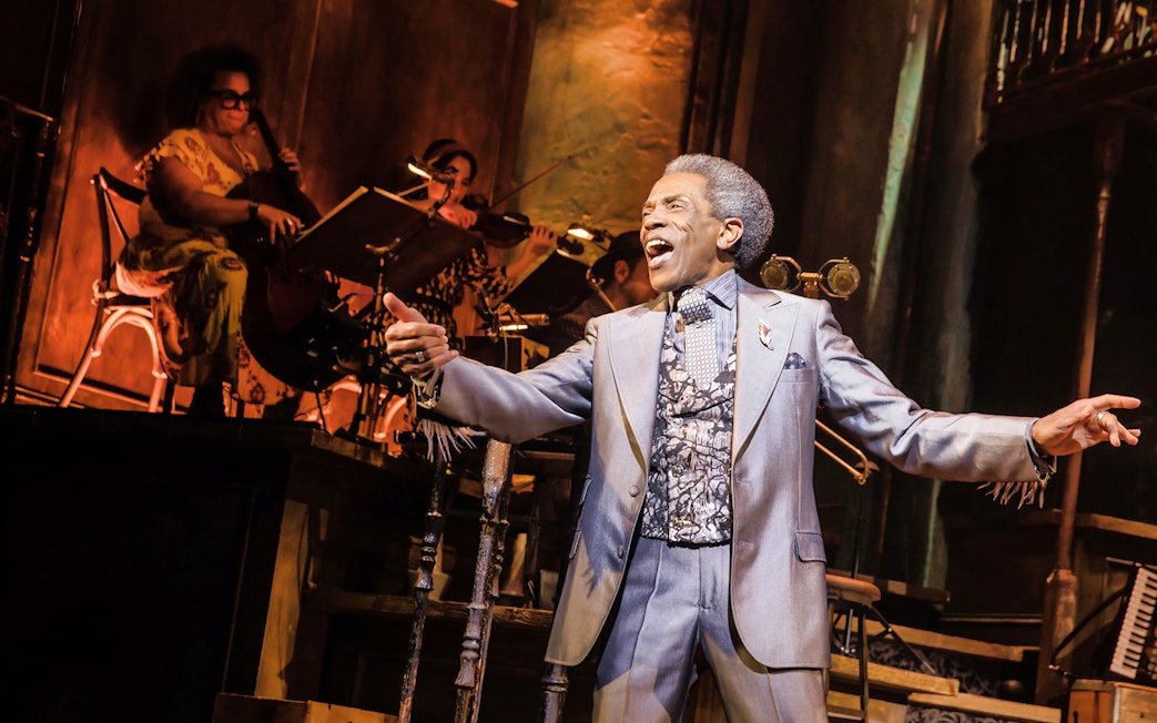 Performer singing on stage during Hadestown musical with musicians in the background.