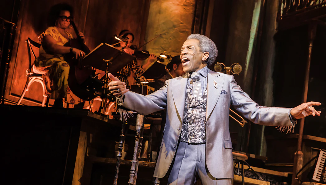 Performer singing on stage during Hadestown musical with musicians in the background.