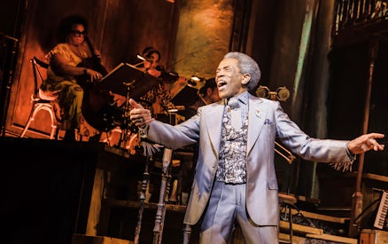 Performer singing on stage during Hadestown musical with musicians in the background.