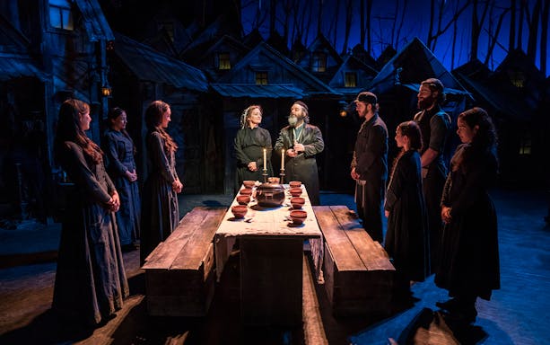 Cast performing a scene from "Fiddler on the Roof" with a table set for a meal.