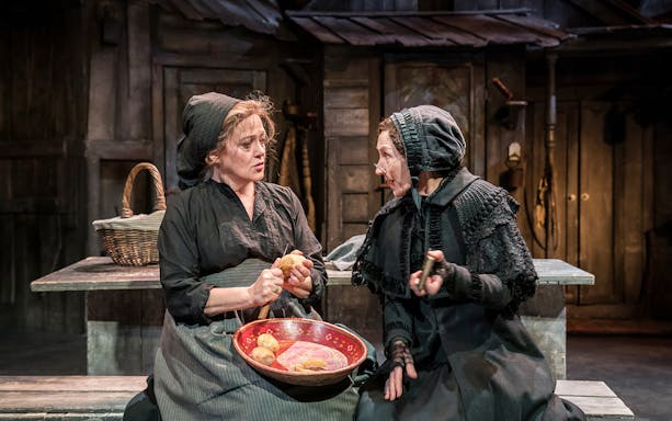 Two women in traditional attire peeling potatoes on stage for Fiddler On The Roof.