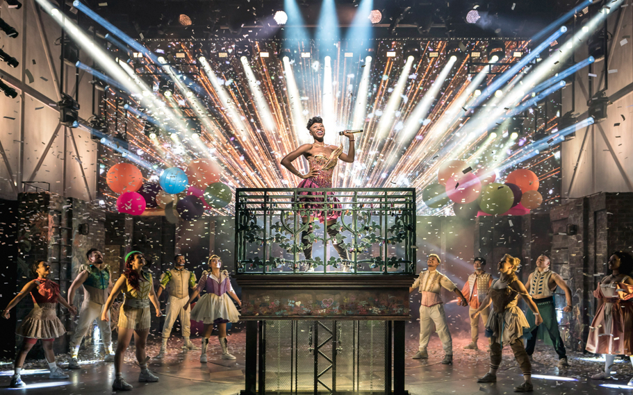 Performer on stage during &Juliet musical with colorful lights and confetti.