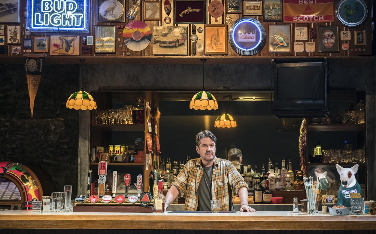 Bar interior with bartender standing behind counter, surrounded by beer taps and vintage decor.