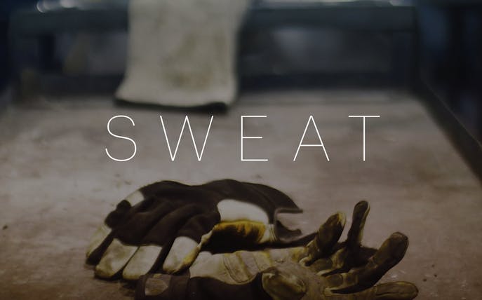 Work gloves on a table with the word "Sweat" in the background.
