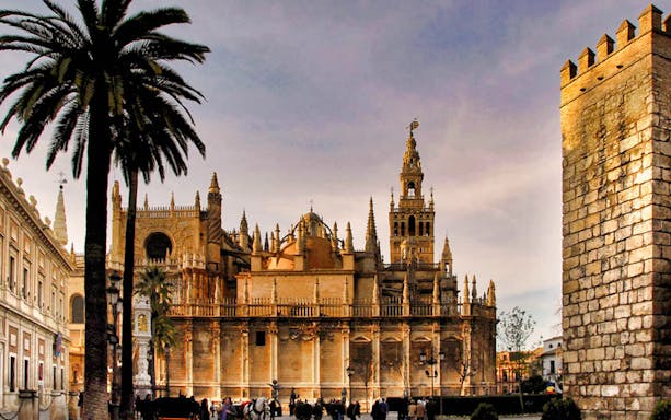 Alcázar, Seville Cathedral, and La Giralda tower with palm trees in foreground.