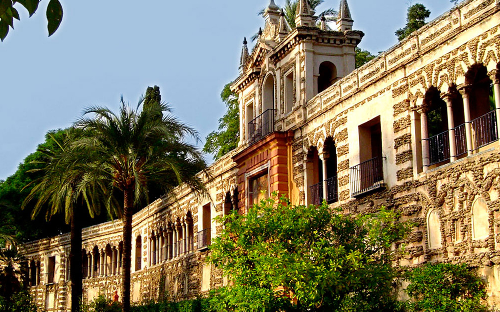 Alcázar of Seville exterior with palm trees and ornate architecture.