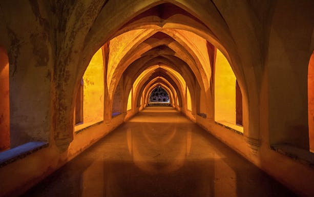 Alcazar of Seville underground arches illuminated during guided tour.