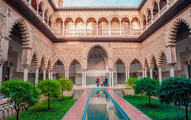 Courtyard of the Alcazar in Seville with intricate arches and reflecting pool.