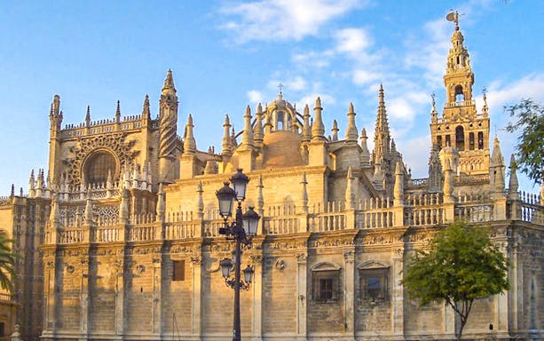 Seville Cathedral exterior with Gothic architecture and Giralda tower in sunlight.