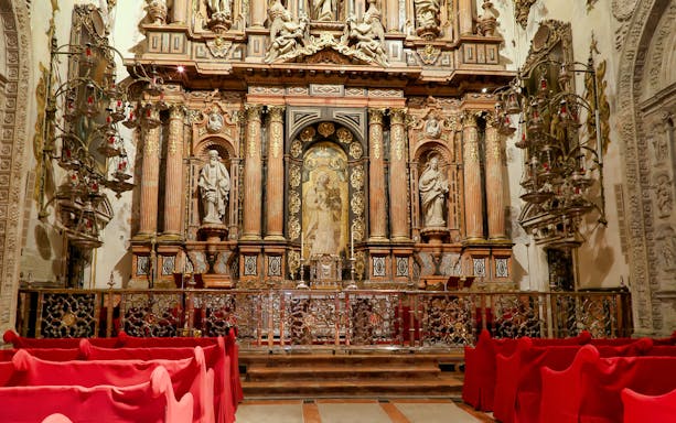 Altar inside Seville Cathedral with ornate carvings and red seating.